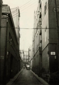 El carrer Miquel Bleach, amb l'escola homònima a la dreta i la fàbrica Hamsa de l'esquerra. Al fons, el carrer Callao (Joan Planàs / AMDSM).